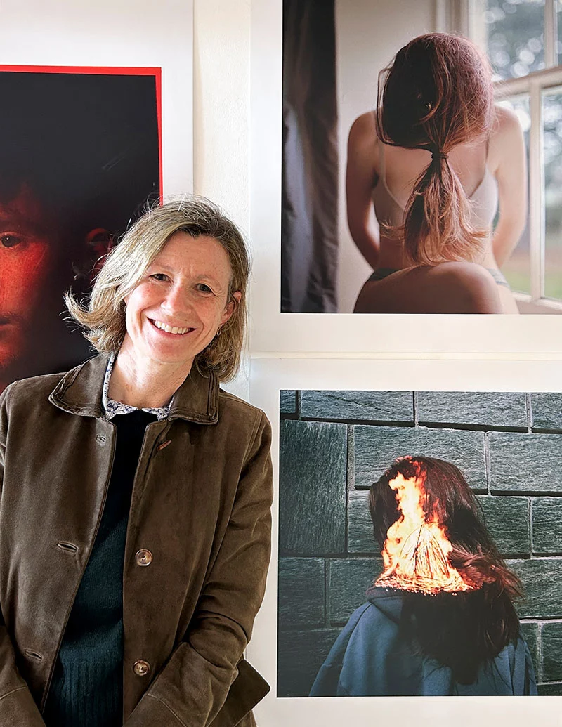 Angela-Crosti-Artist A portrait image of Angela Crosti, pictured in front of prints from her exhibition "You Are Everything to me"